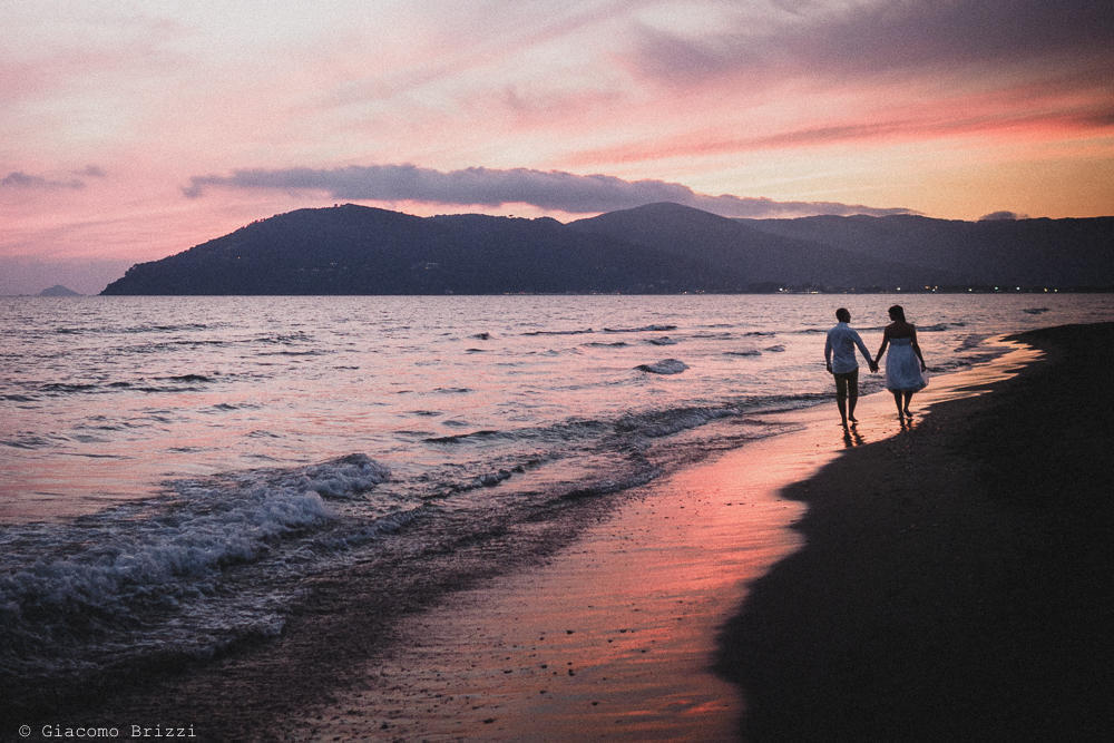 Gli sposi si allontanano lungo la riva del mare al tramonto, fotografo matrimonio Sarzana, Liguria