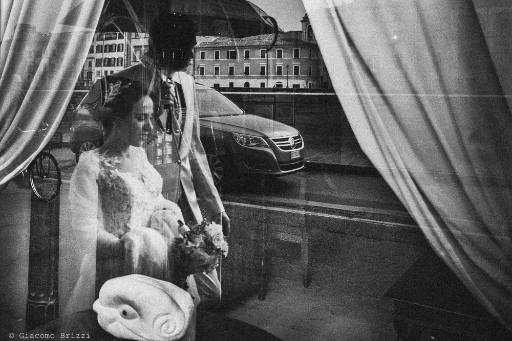 Gli sposi passeggiano ripresi nel riflesso di una vetrina, fotografo ricevimento matrimonio a pisa, palazzo dei dodici